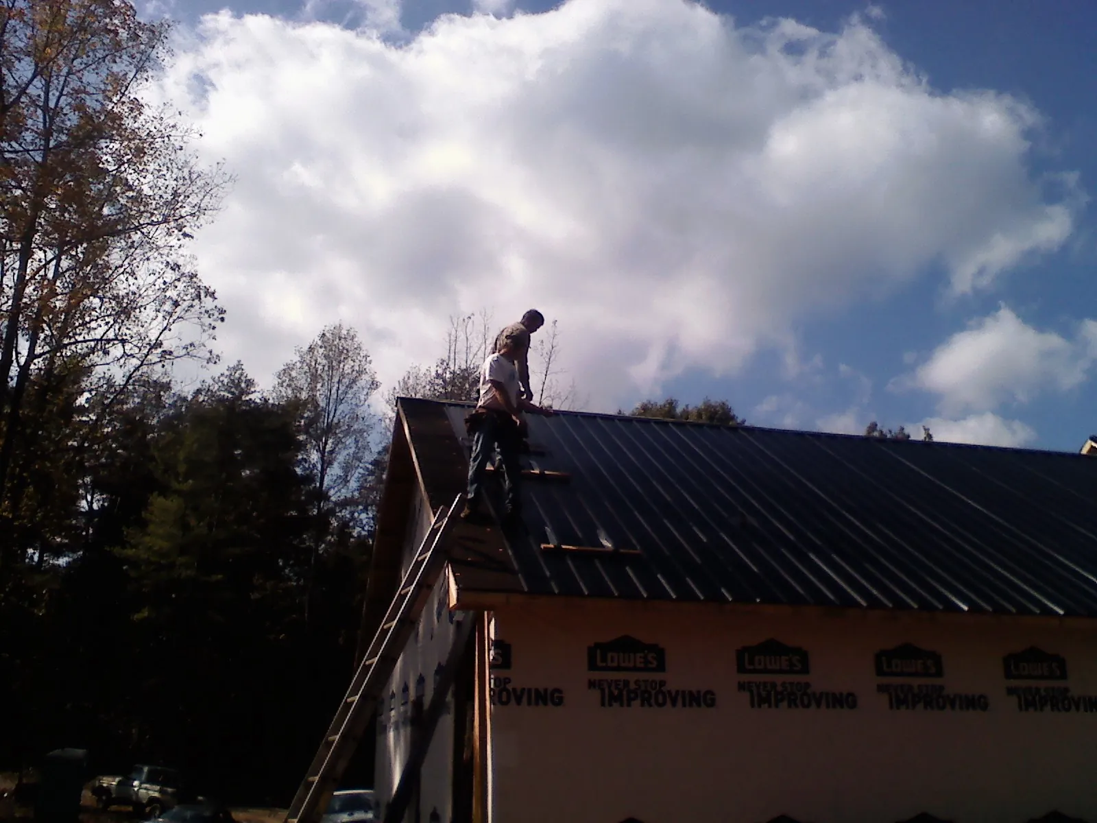 Roofer fastening dark metal panels high against a cloudy sky, from a Roof Inspection job in Baxter